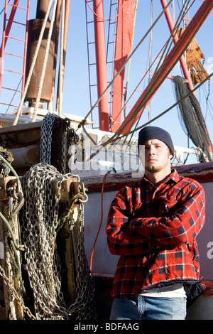 Young fisherman in plaid shirt leaning against fishing boat Stock Photo