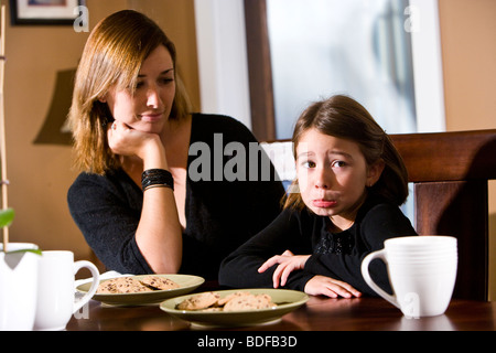 Mother and daughter sitting at dining room table with cookies Stock Photo
