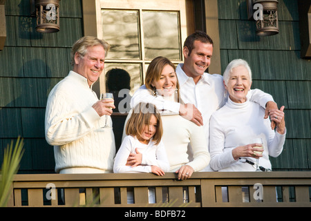 Multi-generational family standing on porch of house with wine Stock Photo