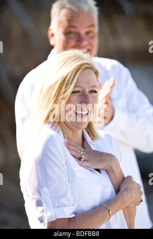 Middle-aged woman laughing while mature man claps in background Stock Photo
