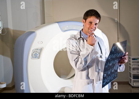 Radiologist holding test results next to CT scanner Stock Photo