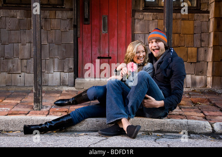 Young affectionate couple sitting on cobblestone sidewalk Stock Photo