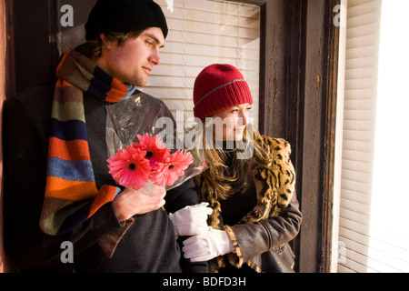 Young couple in warm clothing standing in doorway holding flowers Stock Photo