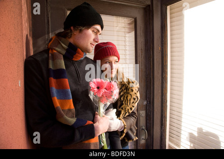 Young couple in warm clothing standing in doorway holding flowers Stock Photo