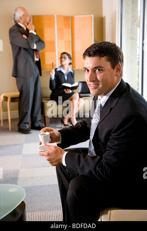 Portrait of businessman drinking coffee with colleagues in background Stock Photo