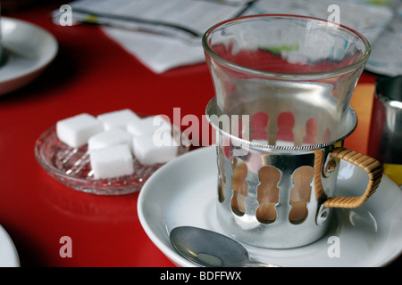 1950s glass cup of tea in aluminium holder with saucer and sugar lumps in Bruges tea room Stock Photo
