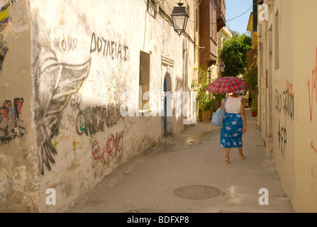 Woman shielding herself from the sun with an umbrella as she walks down a Rethymnon old town alleyway Stock Photo