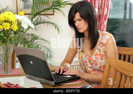 Pretty dark haired young woman using a PC laptop computer in her home. Stock Photo