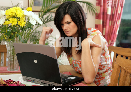 Young dark haired woman using a PC laptop, looking stressed. Stock Photo