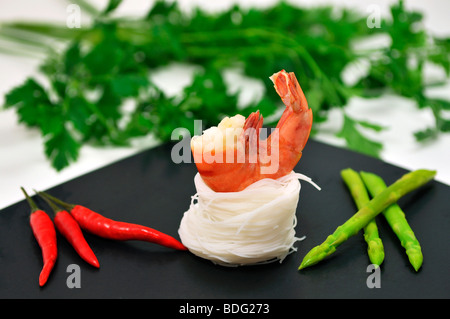Scampi on a bed of rice noodles with Thai asparagus and red chilli in front of parsley Stock Photo