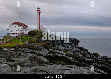 Cape Forchu lighthouse on the Atlantic Ocean with clouds and wet rocks near Yarmouth Nova Scotia Stock Photo