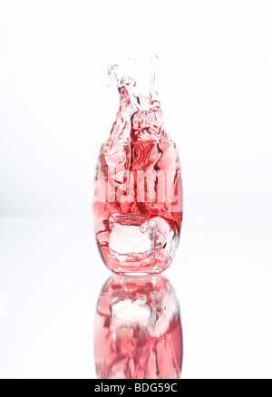 Ice cubes falling into a glass filled with red liquid Stock Photo