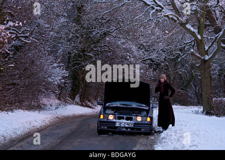 Women on her own with broken down car in the snow,stranded trying to get it fixed. Stock Photo