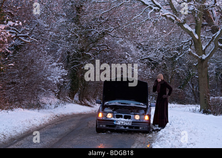 Women on her own with broken down car in the snow,stranded on mobile phone trying to get help to get it fixed. Stock Photo