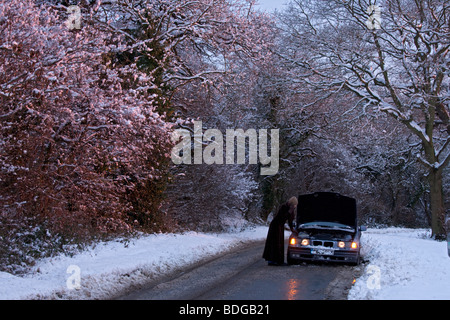 Women on her own with broken down car on country road in the snow, stranded trying to get it fixed. Stock Photo