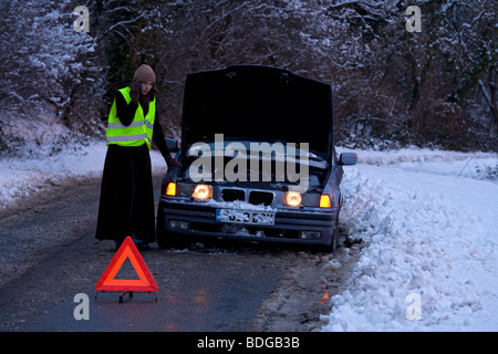 Women on her own broken down in the snow,stranded on mobile phone trying to get help in fluorescent jacket. Stock Photo