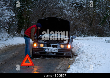 Women on her own broken down in the snow, stranded trying to get it fixed. Stock Photo