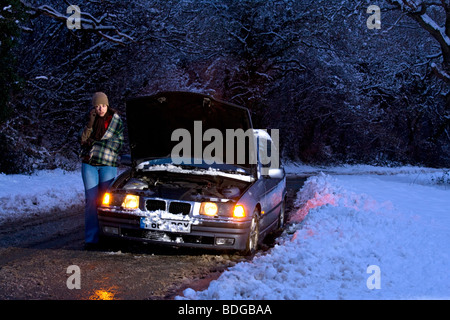 Women on her own broken down in the snow, stranded trying to get it fixed at night, ringing for help. Stock Photo
