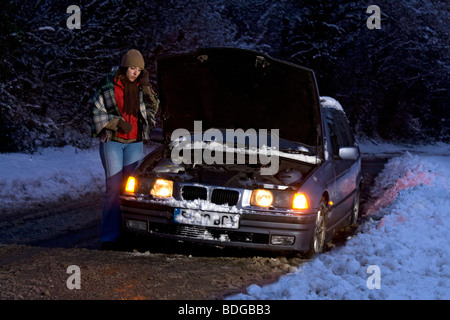 Women on her own broken down in the snow, stranded trying to get it fixed,on mobile phone ringing for help at night. Stock Photo
