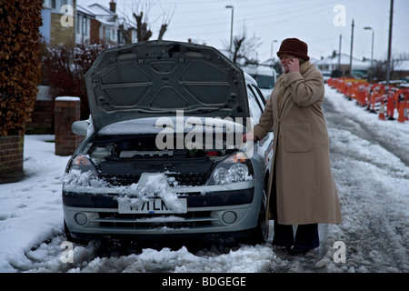 women on her own with broken down car in winter snow, bonnet up on mobile phone to breakdown recovery service Stock Photo