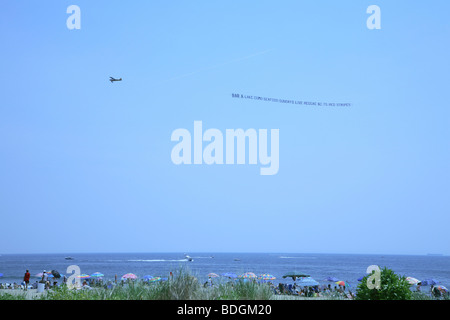 Small airplane dragging a really long transparent advertising banner low over ocean just off new jersey shoreline. Stock Photo