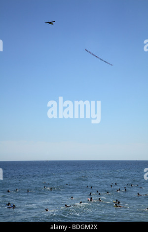 Airplane dragging advertising banner low over water full of swimmers Stock Photo