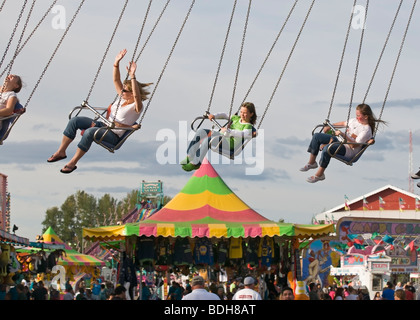 People at the county fair fly high in a chain swing ride over the fairgrounds. Stock Photo