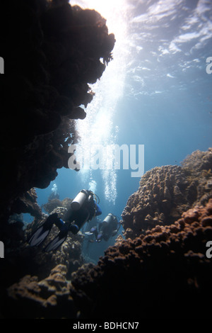 Scuba divers swimming out of an underwater cave Stock Photo