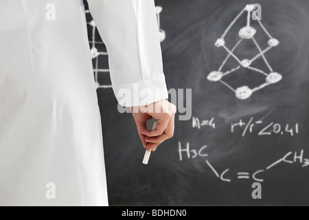 rear view of woman in lab clothes writing chemical formula on blackboard Stock Photo