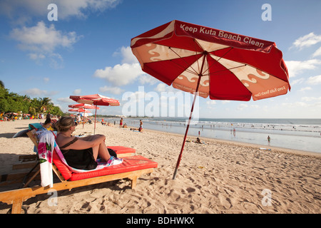 Indonesia, Bali, Kuta, beach, woman sitting on lounger in shade of Keep Kuta Beach Clean parasol Stock Photo