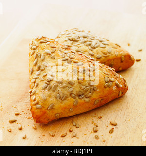 Two triangular shaped fresh rustic bread rolls on a wooden bread board. Stock Photo