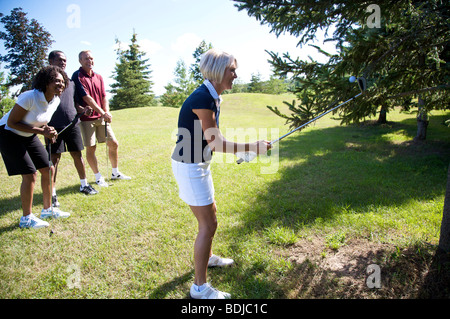Group of Golfers Watching Woman Try to Retrieve Golf Ball From a Tree Stock Photo