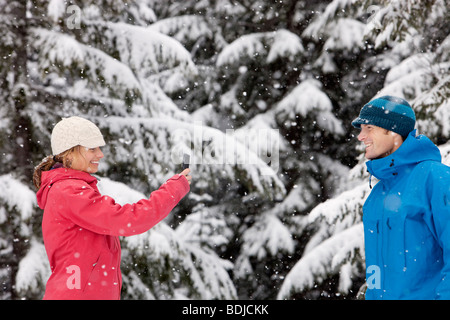 Woman Taking Picture of Man with Camera Phone Outdoors in Winter, Whistler, British Columbia, Canada Stock Photo