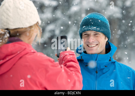 Woman Taking Picture of Man with Camera Phone Outdoors in Winter, Whistler, British Columbia, Canada Stock Photo