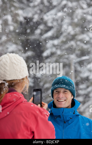 Woman Taking Picture of Man with Camera Phone Outdoors in Winter, Whistler, British Columbia, Canada Stock Photo