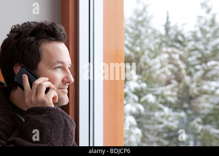 Man in Bathrobe Talking on Cell Phone and Looking Out the Window Stock Photo