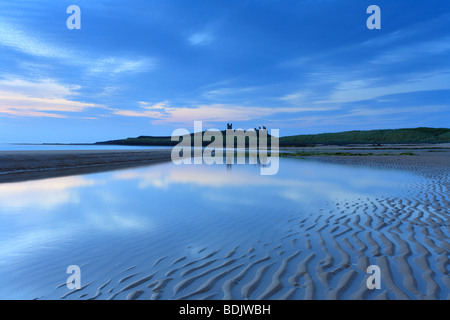 Dawn Embleton Bay, Dunstanburgh Castle on the horizon. Sunrise Northumberland coastal scene, reflections in pool. Stock Photo