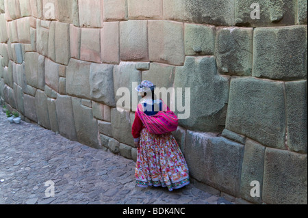 Indian woman on cobble stone street lined with Inca walls of polygonal stones, Cuzco, Peru
