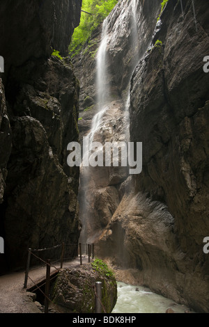 Beautiful tall waterfall against steep rock face in Partnachklamm gorge of Garmisch-Partenkirchen swift mountain stream below Bavaria Germany EU Stock Photo