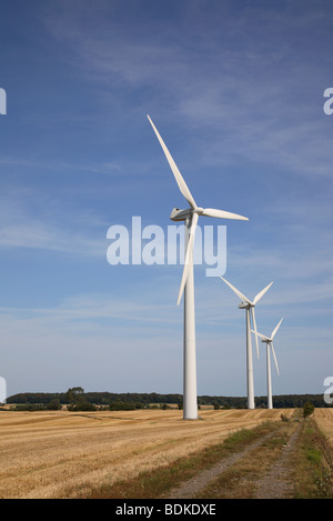 Three wind turbines on a field against a blue sky on a sunny day in the late summer. On the island Møn in Denmark. Sustainability. Stock Photo