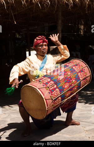 Indonesia, Lombok, Sade, traditional Sasak village, man drumming to welcome visiting party of tourists Stock Photo