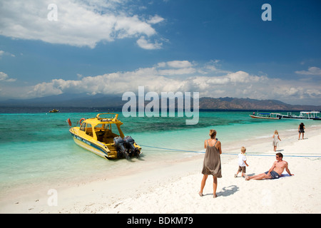 Indonesia, Lombok, Gili Trawangan beach, family walking along beach past young man sunbathing Stock Photo