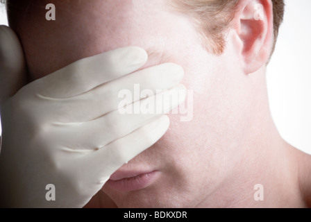 Man covering his eyes while wearing a white medical glove Stock Photo