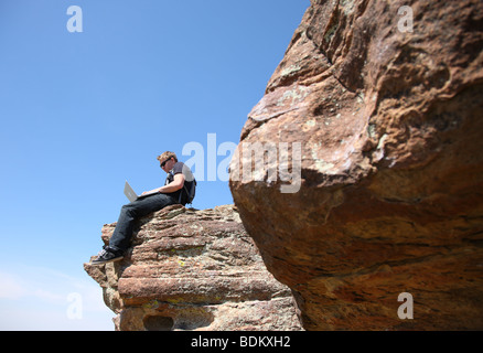 Young man using laptop on cliff Stock Photo