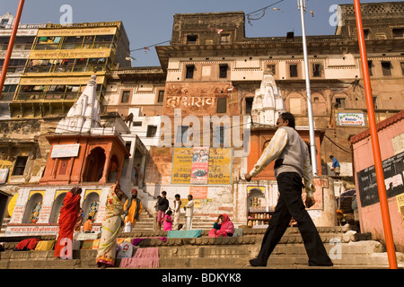 A man strides along the ghats of Varanasi, India. Men and women stand and look at the walking man. Stock Photo