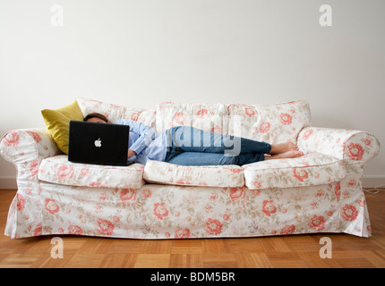 Young woman lying on sofa at home working with a laptop computer Stock Photo