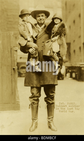 Circa 1920 postcard, 'Col. Parks, Tallest soldier in the last big World War.' He is holding two well-dressed Little People. Stock Photo