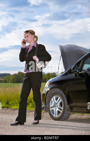 Woman dressed in business attire using cellphone on rural road, after car breakdown, Manitoba, Canada Stock Photo