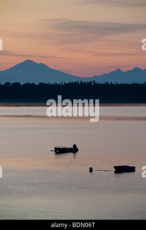 At sunrise looking out over Hales Pass two boats are anchored offshore. Mt. Baker and the Sisters Mountains in the background. Stock Photo