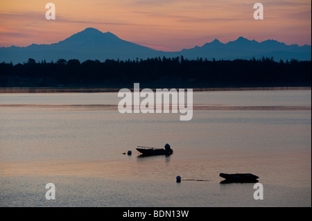 At sunrise looking out over Hales Pass two boats are anchored offshore. Mt. Baker and the Sisters Mountains in the background. Stock Photo